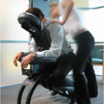 Corporate massage therapist performing seated chair massage in an office workplace.